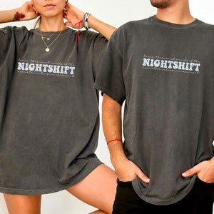 May include: Two charcoal gray t-shirts with the text "...know these sweet sounds of the NIGHTSHIFT...neonatal intensive care unit" in a white, stylized font. The shirts are worn by two people.