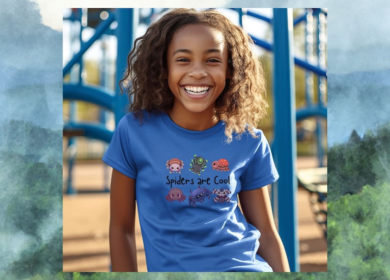 Pode incluir: Uma camiseta azul com um gr&aacute;fico de aranhas de desenho animado e o texto "Spiders are Cool". A camiseta est&aacute; sendo usada por uma pessoa sorrindo, com uma estrutura de playground azul ao fundo.