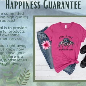 May include: A magenta t-shirt with a cartoon spider illustration and the text "a little bit scary a whole lot cute." The shirt is paired with blue jeans, a pink flower, and black sandals. The image also includes text about a happiness guarantee.