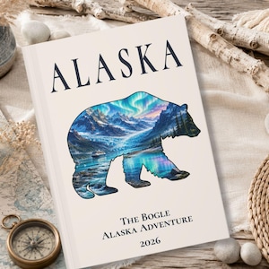 May include: A rectangular book with a cream-colored cover featuring the word ALASKA in black text at the top. A silhouette of a bear contains a colorful landscape of mountains, a glacier, and the aurora borealis. Text reads The Bogle Alaska Adventure 2026.