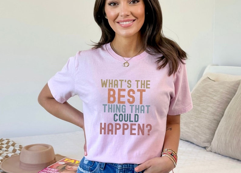 Puede incluir: Una camiseta rosa con el texto "What's the best thing that could happen?" en letras de colores.