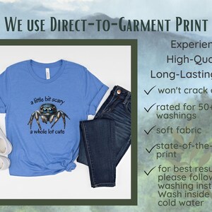May include: A light blue t-shirt with a graphic of a jumping spider and the text "a little bit scary a whole lot cute." The shirt is paired with dark blue jeans and white sneakers. The image also includes text about the printing process.
