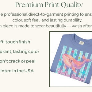 May include: A periwinkle blue t-shirt featuring a graphic of a pink whale swimming over vertical teal stripes and colorful stars. The text "Hello there!" is printed in pink below the whale. The image includes text about premium print quality.