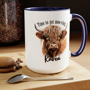 May include: White ceramic mug with a blue rim and handle. The mug features a brown and white Highland cow with the text "Time to get moo-ving" and the name "Karen" printed on the front.