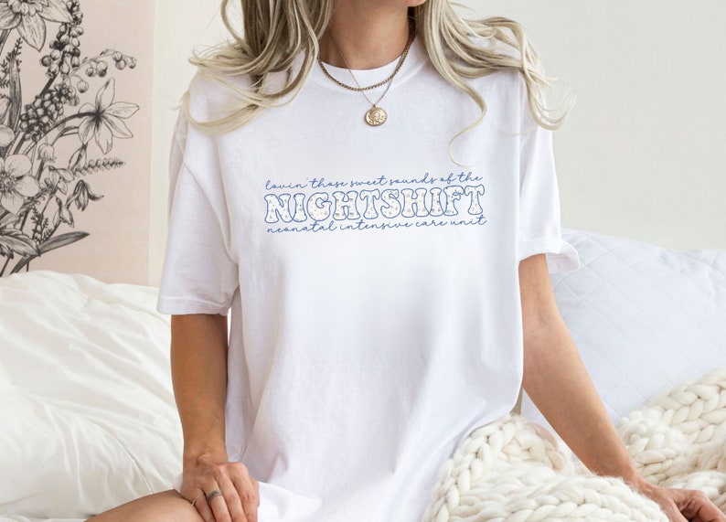 May include: White t-shirt with blue text that reads "Lavin' those sweet sounds of the NIGHTSHIFT neonatal intensive care unit." The shirt has a relaxed fit and is made of a soft material.