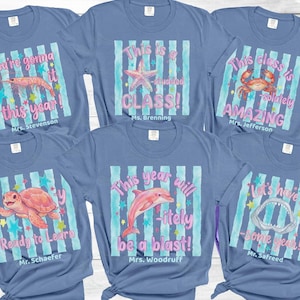 May include: Six blue short-sleeve t-shirts featuring watercolor-style sea creatures, light blue vertical stripes, and colorful stars. Each shirt displays unique text puns and teacher names, including shrimp, starfish, crab, turtle, dolphin, and shark.