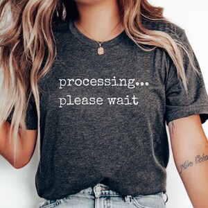 May include: A dark gray t-shirt with the text "processing... please wait" printed in white.
