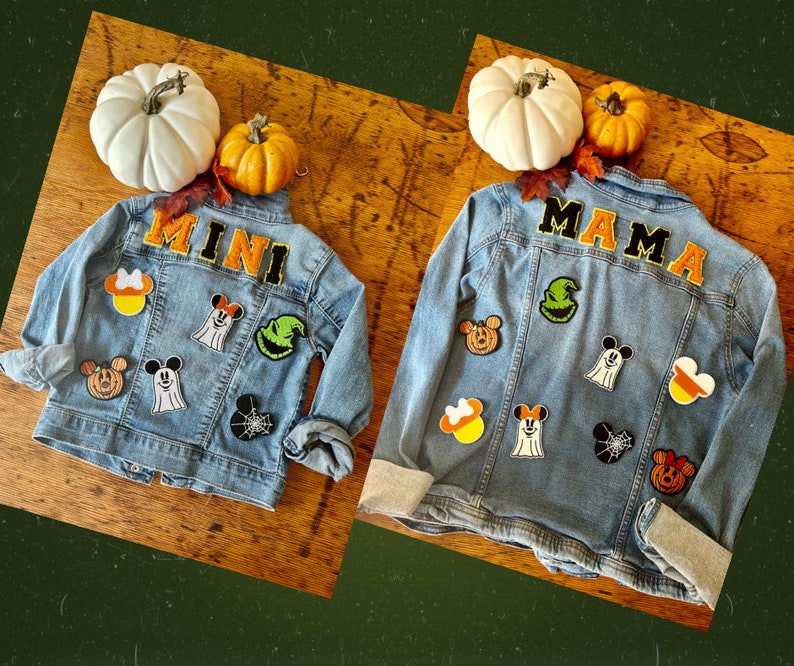 May include: Two light blue denim jackets decorated with embroidered patches. One jacket features the word MINI, the other MAMA. Both include patches of ghosts, pumpkins, spiderwebs, and candy corn, all styled with iconic mouse-ear silhouettes.