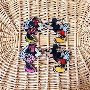 May include: Four embroidered iron-on patches featuring Mickey Mouse and Minnie Mouse in various poses. The patches are on a woven wicker background.