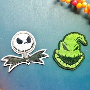 May include: Two embroidered iron-on patches featuring the faces of Jack Skellington from The Nightmare Before Christmas and the Grinch from How the Grinch Stole Christmas. The patches are on a blue background.