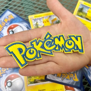 May include: A yellow and blue embroidered patch with the word "Pokemon" in a stylized font.