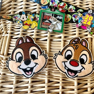 May include: Two brown and white embroidered Chipmunk character patches with smiling faces. The patches are on a woven wicker background.
