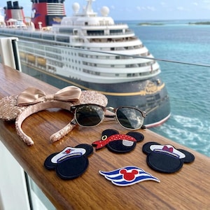May include: A rose gold sequined Minnie Mouse ear headband with a matching bow, sunglasses, and Mickey Mouse-themed patches on a wooden surface, with a cruise ship and ocean in the background. The patches include Mickey Mouse hats and a Disney cruise logo.
