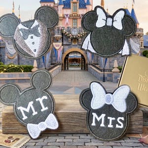 May include: Four gray Mickey Mouse head-shaped wedding decorations. Two are designed as a bride and groom, and two read "Mr" and "Mrs" with bow ties. A gold box with "Disneyland Weddings" is visible in the background.