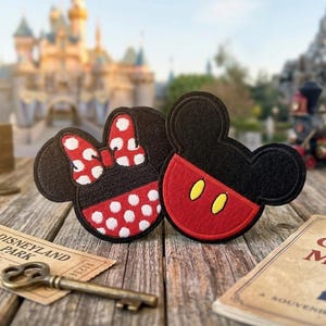 May include: Two embroidered patches in the shape of Mickey and Minnie Mouse heads. Minnie has a red and white polka dot bow and skirt. Mickey has a red bottom with two yellow ovals. Disneyland Park ticket and key.