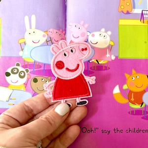 May include: A pink Peppa Pig patch with a red dress is held in front of a colorful illustration from a children's book. The book features other cartoon characters and the text "Ooh!" say the children.
