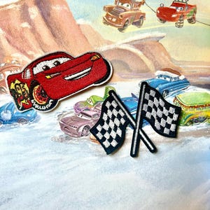 May include: A red cartoon race car with a checkered flag. The car is on a page from a children's book with other cartoon cars.