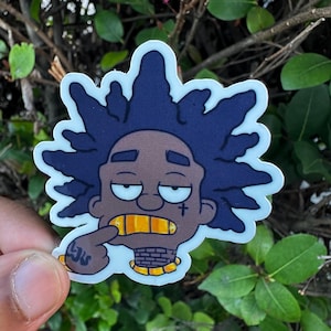 May include: A cartoon sticker featuring a stylized face with dark skin, blue hair, and gold teeth. The character is pointing at their gold teeth with a finger. The sticker has a white border and a small tattoo on the hand.