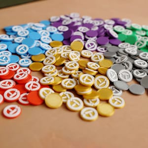 May include: A collection of colorful game tokens in red, orange, yellow, green, blue, purple, and gray. Each token has a white letter "T" in the center.