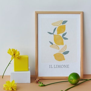 Könnte beinhalten: Ein gerahmter Druck mit einer stilisierten Illustration von Zitronen und dem Text "IL LIMONE". Der Druck ist auf weißem Hintergrund und in einem naturfarbenen Holzrahmen gerahmt. Der Druck steht auf einem Tisch mit einer gelben Box und einem weißen Würfel.
