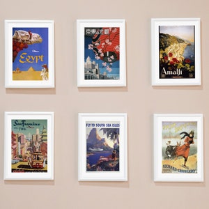 May include: Six vintage travel posters in white frames on a beige wall. The posters feature destinations like Egypt, Tokyo, Amalfi, San Francisco, South Sea Isles, and a winter scene.