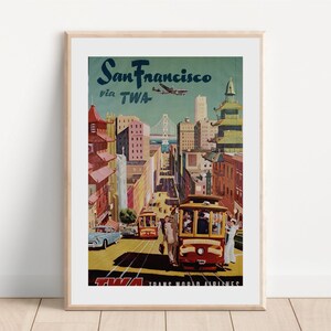 May include: Vintage travel poster advertising a trip to San Francisco via TWA airlines. The poster features a colorful illustration of the city skyline, including the Golden Gate Bridge, cable cars, and buildings. The text "San Francisco via TWA" is prominently displayed at the top of the poster.