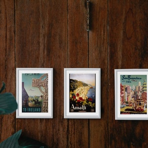 May include: Three framed vintage travel posters on a wooden wall. The posters feature images of a cross in Ireland, a coastal town in Amalfi, and a cityscape of San Francisco.