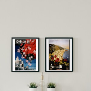 May include: Two framed vintage travel posters. The poster on the left features a red lantern with cherry blossoms and the text "Tokyo no Hikari" in Japanese. The poster on the right features a scenic view of Amalfi, Italy with the text "Amalfi" in white.