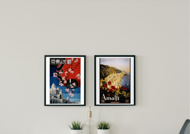 May include: Two framed vintage travel posters. The poster on the left features a red lantern with cherry blossoms and the text "Tokyo no Hikari" in Japanese. The poster on the right features a scenic view of Amalfi, Italy with the text "Amalfi" in white.
