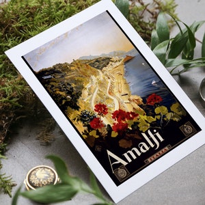 May include: A vintage travel poster featuring a scenic view of Amalfi, Italy. The poster is printed on white cardstock and features a colorful illustration of a coastal town with a winding road leading up a hillside. The text "Amalfi" is printed in bold, black letters at the bottom of the poster.