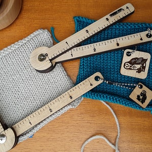 May include: Two wooden knitting gauge tools with a ruler and a rotating dial. The tools are placed on top of two knitted fabric swatches, one in a light grey colour and the other in a teal blue colour. The swatches are attached to wooden tags with a small owl and a bear design. The text "Patent pending" is visible in the bottom right corner of the image.