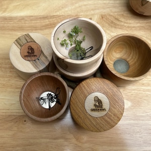 May include: Wooden bowls and lids with the "GREEN OWL" logo. The bowls are various sizes and shapes, some with contents like greenery and small objects. The lids feature a circular design with an owl illustration.