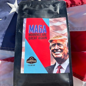May include: A black coffee bag with a red, white, and blue design. The bag features a portrait of Donald Trump and the text "Maga Mornings Are Great Again". The bag also includes the text "The Lawman" and "12 oz Net Wt".