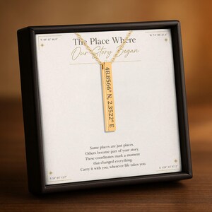 May include: A gold-toned vertical bar pendant necklace featuring the engraved coordinates 48.8566 N, 2.3522 E. The necklace is displayed on a white card inside a black box, with the text The Place Where Our Story Began printed above the pendant.