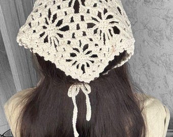 May include: Cream-colored crochet hat with a floral design. The hat is tied at the back with a bow. The hat is worn on the head.