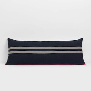 May include: A long, navy blue pillow with two white stripes. The pillow has a zipper closure.
