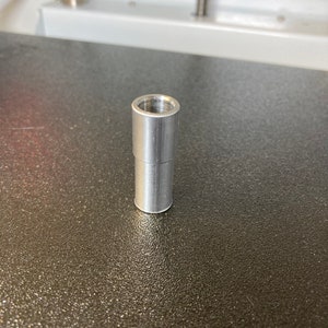 Puede incluir: Un conector de metal plateado con una abertura roscada en la parte superior.