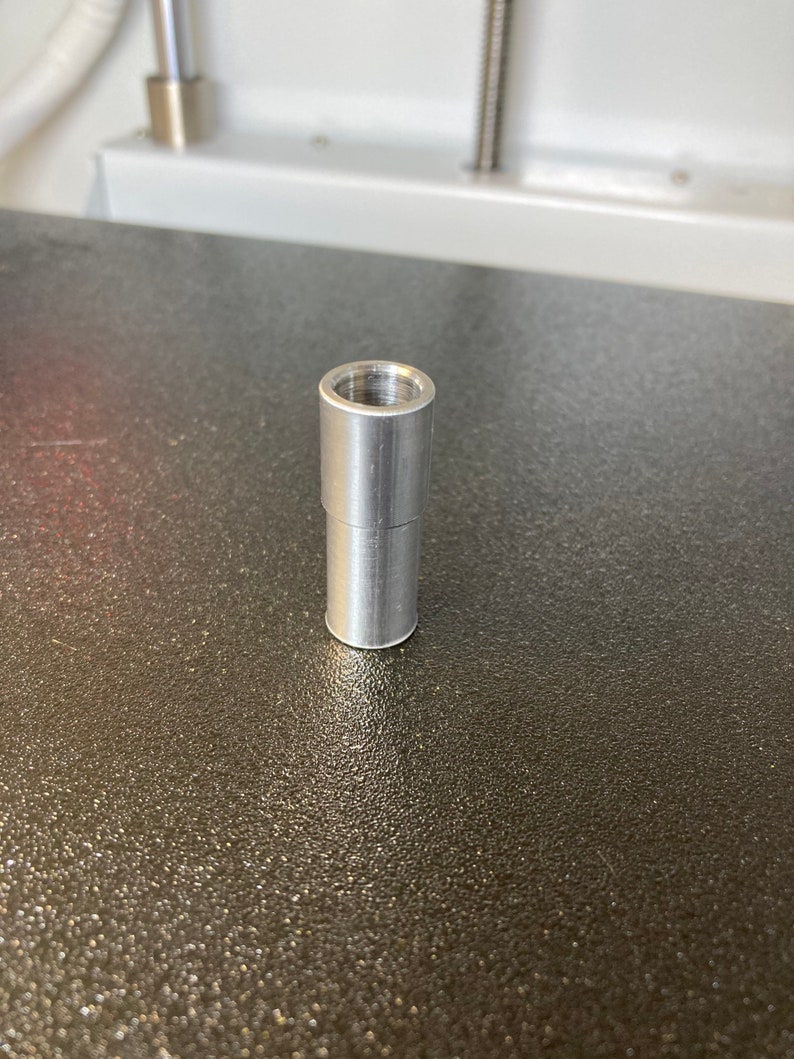 Puede incluir: Un conector de metal plateado con una abertura roscada en la parte superior.