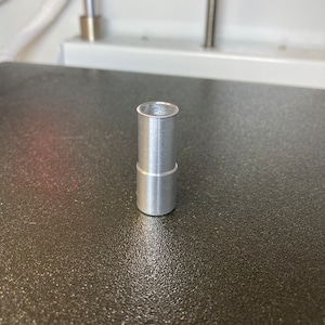 Puede incluir: Un tubo de metal plateado con un acabado liso cepillado. El tubo mide aproximadamente 5 cm de largo y tiene un di&aacute;metro de unos 2,5 cm.