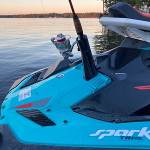 May include: A blue and black jet ski with a fishing rod attached to the front. The jet ski has the word 'spark' and 'TRIXX' written on the side. The jet ski is in the water and the fishing rod is pointing towards the sky.