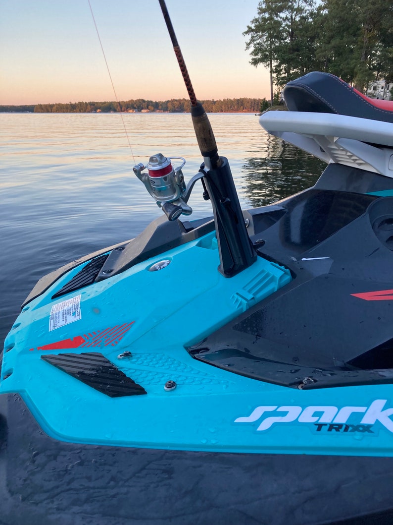 May include: A blue and black jet ski with a fishing rod attached to the front. The jet ski has the word 'spark' and 'TRIXX' written on the side. The jet ski is in the water and the fishing rod is pointing towards the sky.