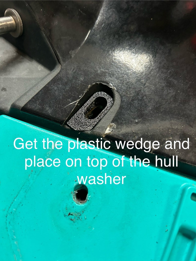 May include: A close-up of a black plastic wedge placed on top of a turquoise surface. The text 'Get the plastic wedge and place on top of the hull washer' is visible below the wedge.