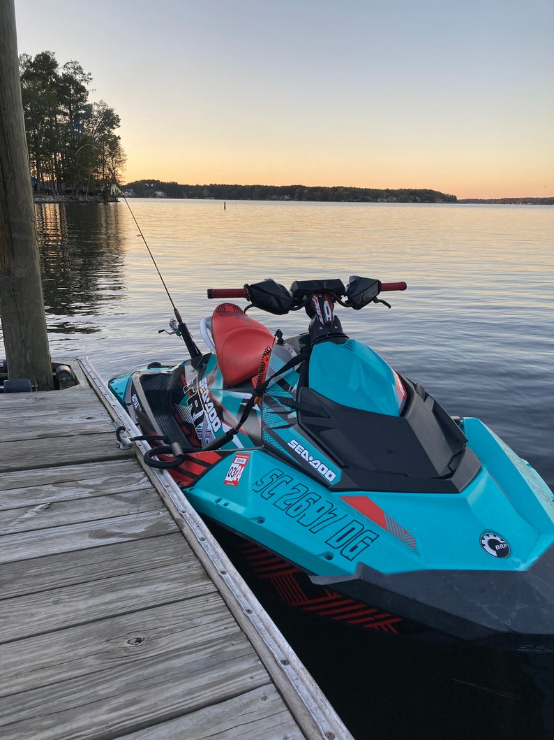 May include: A turquoise and black Sea-Doo Spark watercraft with red and white accents. The watercraft has the text 'Sea-Doo' and 'Spark' on the side and 'SC 2677 DG' on the front. The watercraft is docked at a wooden pier.