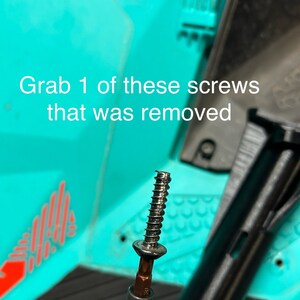 May include: A silver screw with a black head is attached to a black screwdriver. The screw is partially threaded. The screw is against a turquoise background.