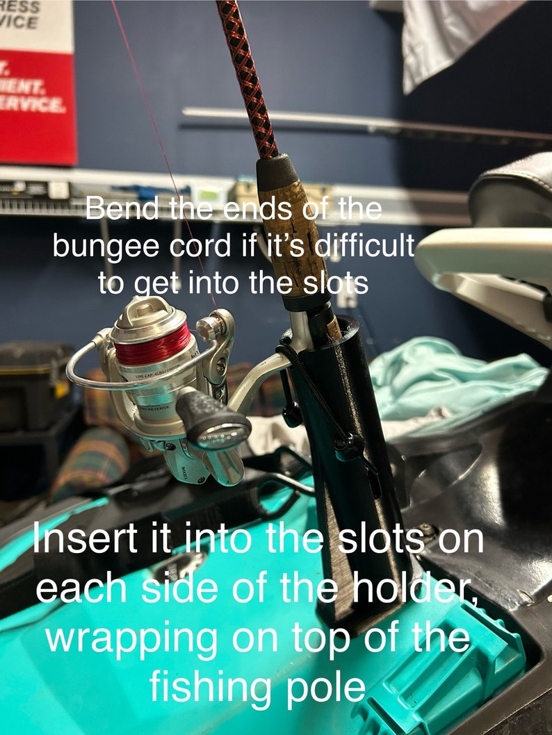 May include: A fishing rod with a reel attached to it is being inserted into a black holder. The holder has two slots on each side and is attached to a turquoise surface. The text on the image reads: 'Bend the ends of the bungee cord if it's difficult to get into the slots' and 'Insert it into the slots on each side of the holder, wrapping on top of the fishing pole.'