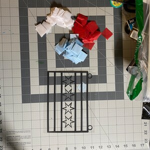 May include: A black silhouette of a Chicago flag with five white stars on a white background. The flag is surrounded by red, white, and blue tissue paper squares.