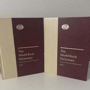 May include: Two hardcover books titled "The World Book Dictionary" with maroon covers and cream-colored spines. The books are labeled "L-Z" and "A-K" and feature a globe logo. The books are on a white surface.