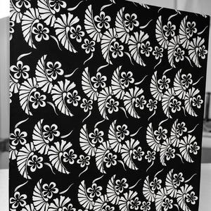 May include: A rectangular fabric panel featuring a high-contrast black background with a repeating white floral pattern. The design consists of stylized five-petaled flowers paired with fan-shaped leaf motifs arranged in horizontal rows.