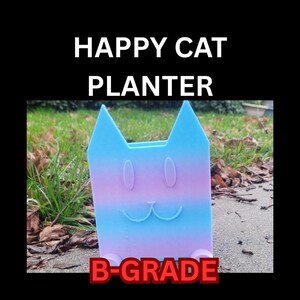 May include: A cat-shaped planter with a gradient of blue and purple hues. The planter has a smiling face and the text "HAPPY CAT PLANTER" and "B-GRADE". The planter is sitting on a concrete surface.