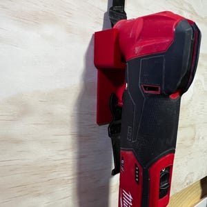 Könnte beinhalten: Ein rot-schwarzes Milwaukee Oszillations-Multitool mit einer schwarzen Klinge, die an einem roten Halter befestigt ist. Das Werkzeug ist auf einer hellen Holzoberfläche montiert. Das Milwaukee-Logo ist auf dem Werkzeugkörper sichtbar.